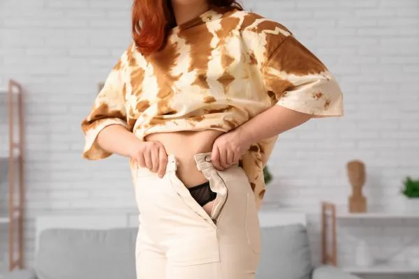 Image of woman trying to do her trousers up after pregnancy weight gain Burgess Hill